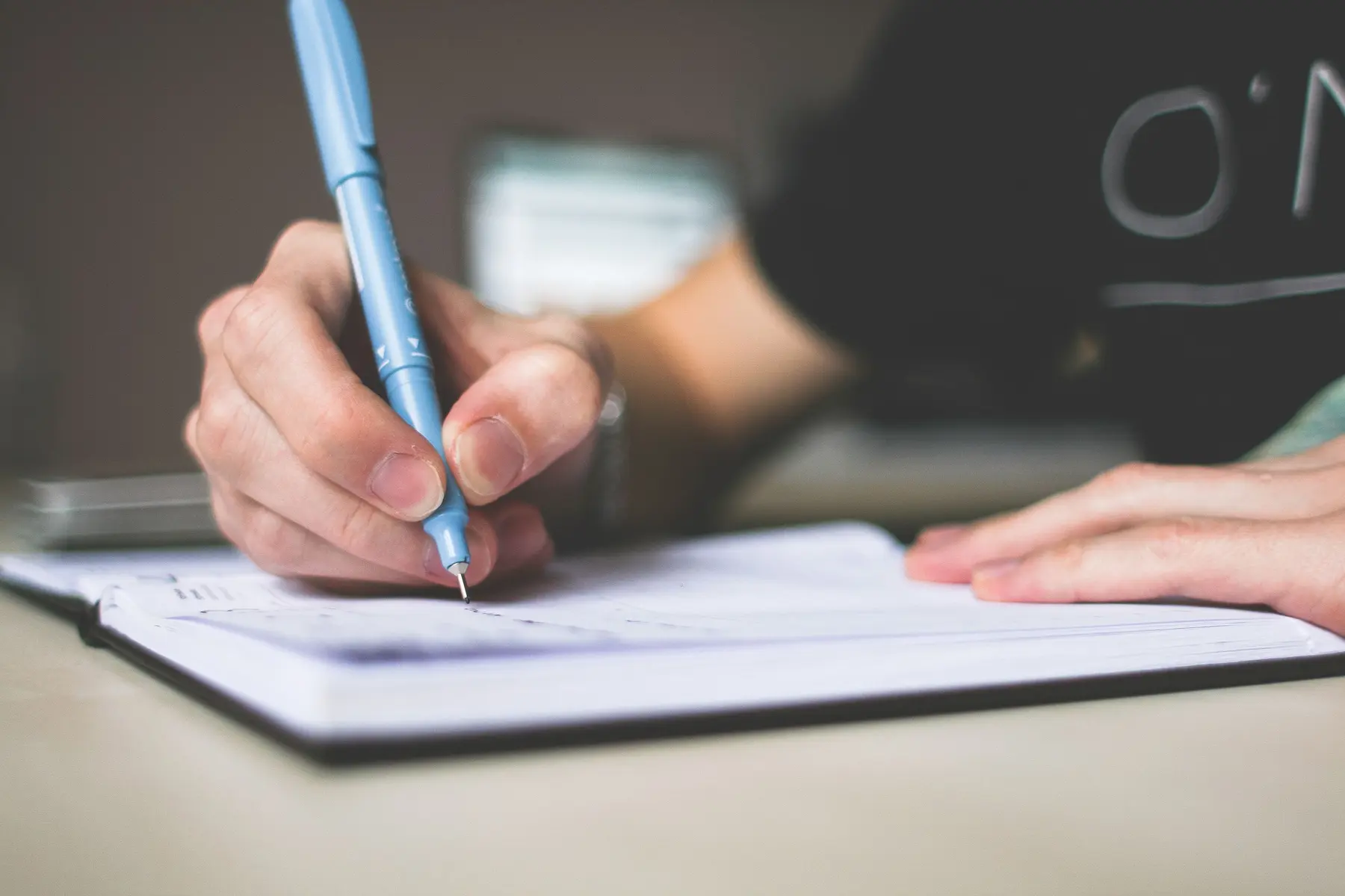 Une main prend des notes dans un carnet avec un stylo bleu